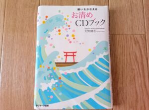 書籍「願いをかなえるお清めCDブック」の表紙。水色の波模様とピンク色の鳥居のイラストが描かれている。
