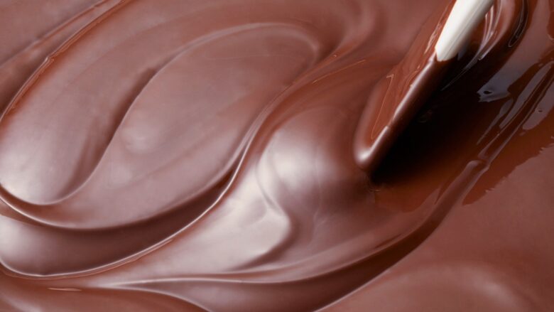 溶かしたチョコレートを白いスパチュラで混ぜる様子。艶やかな質感と渦巻く模様が特徴