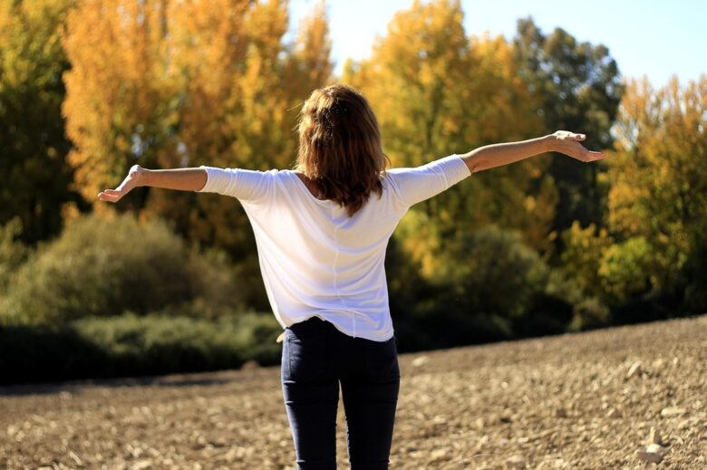 自然の中で両手を広げ、清々しい空気を感じる女性の後ろ姿。香りに悩まされず、自分も周りも心地よくいられる毎日を表すイメージ。
