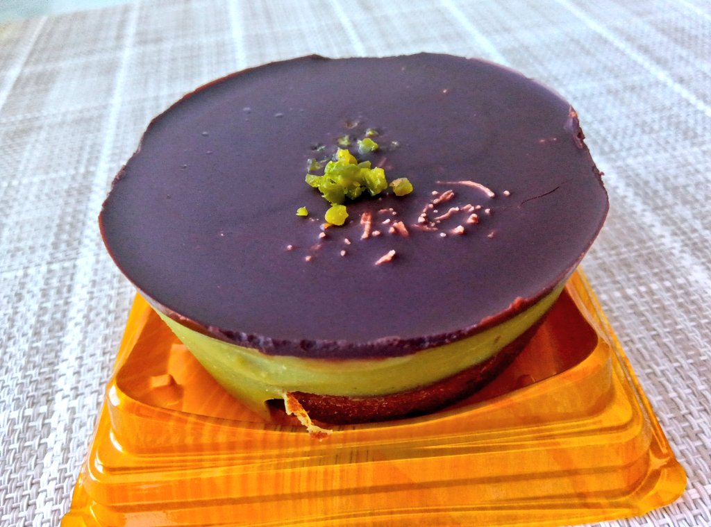成城石井の『ドバイチョコ風ケーキ』。濃厚なチョコレート層の下に、ザクザク食感のガダイフとピスタチオクリームが重なった美しい断面。仕上げに刻んだピスタチオが散りばめられた、贅沢なスイーツ