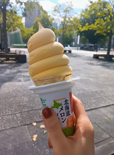 セイコーマートのメロンソフトを手にした帯広の朝。公園のベンチと木々が背景に