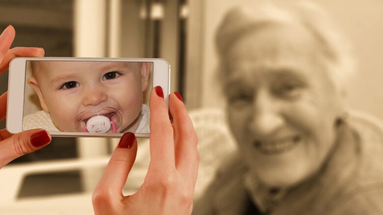 スマートフォンに映る赤ちゃんの写真と、背景にぼんやりと映る笑顔の高齢者。世代を超えたつながりと、肌の記憶を象徴するイメージ。