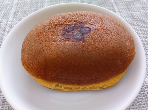 白い皿に乗せられた、ハタダ「どら一 焼き芋カスタード」。こんがりときれいな焼き色がついたふっくらとした生地で、中央には花の形の焼印が押されている。