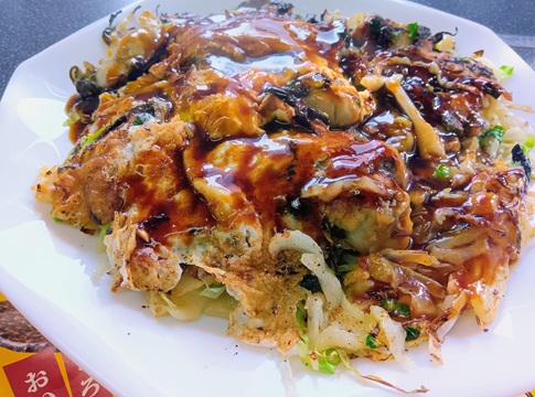 岡山備前市日生（ひなせ）名物、牡蠣がゴロゴロ入ったB級グルメ「カキオコ」。ソースがたっぷりかかった鉄板焼きの写真。