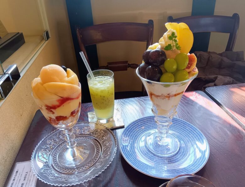 倉敷美観地区のカフェ「くらしき桃子」で提供される2種のフルーツパフェ。白桃と巨峰・マスカットが贅沢に盛られ、キウイジュースと紅茶とともにテーブルに並ぶ。